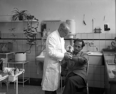 821218 Afbeelding van een arts die een werknemer verbindt in de behandelkamer van de Medische Dienst van de N.V. ...